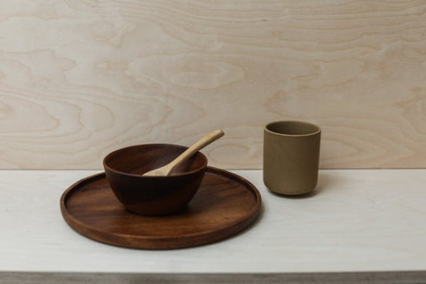 A Wooden Bowl on a Wooden Plate Near the Ceramic Cup on the Table
