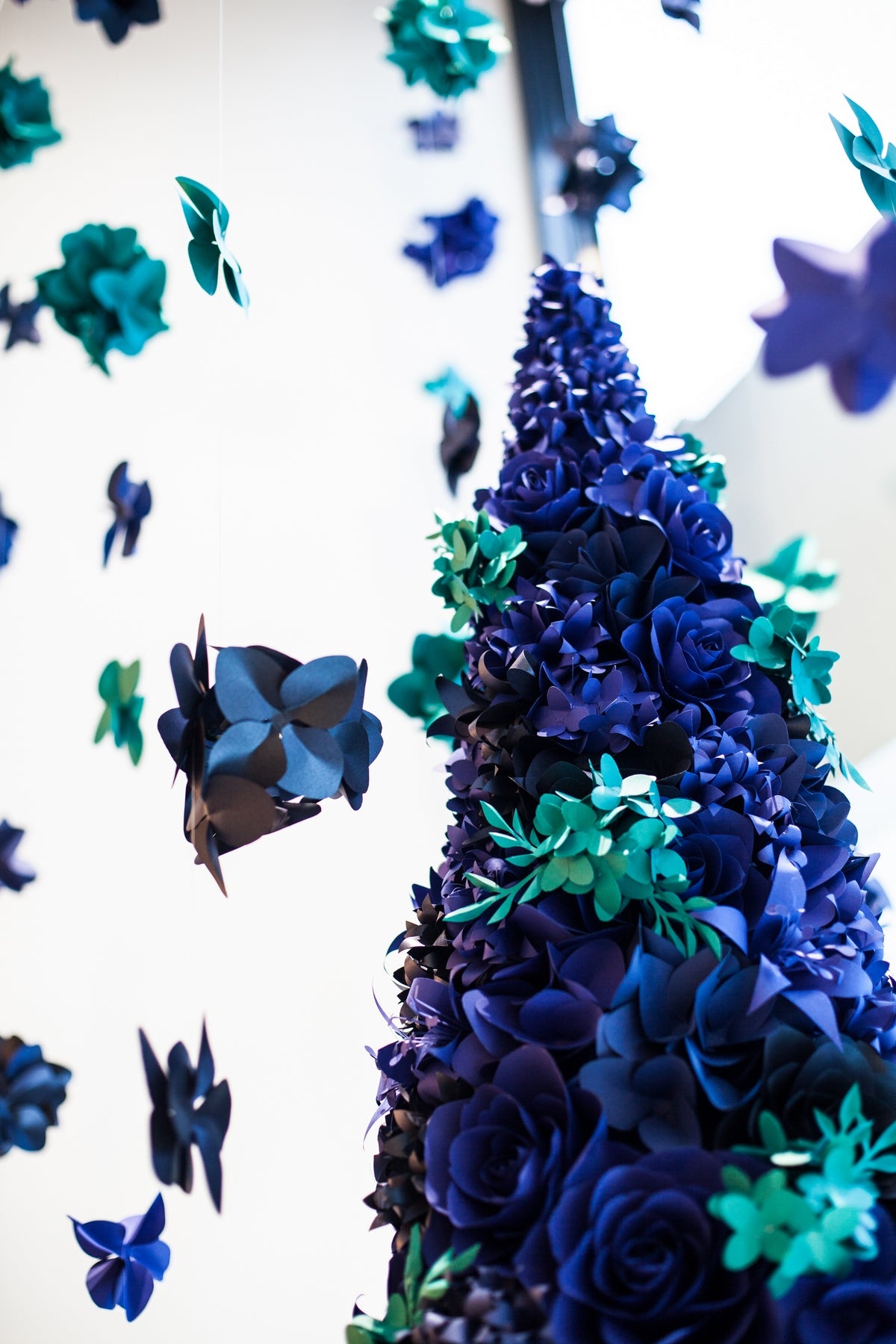 Mesmerizing installation of a paper flower Christmas tree, adorned with intricate ultramarine blue and turquoise blue paper flowers, evoking a sense of enchantment and joy during the holiday season.