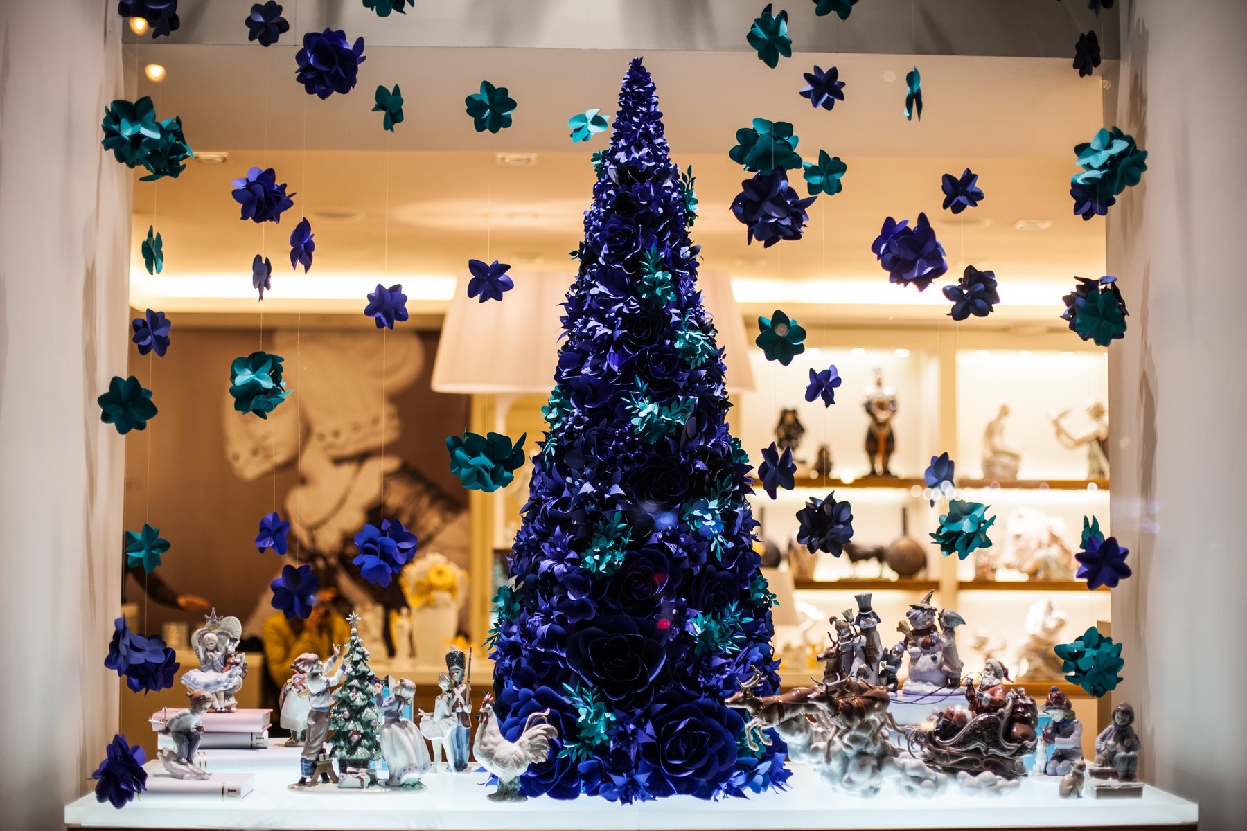 Eye-catching winter display featuring a meticulously crafted paper flower Christmas tree in stunning shades of ultramarine blue and turquoise blue, accented by cascading paper hydrangeas.