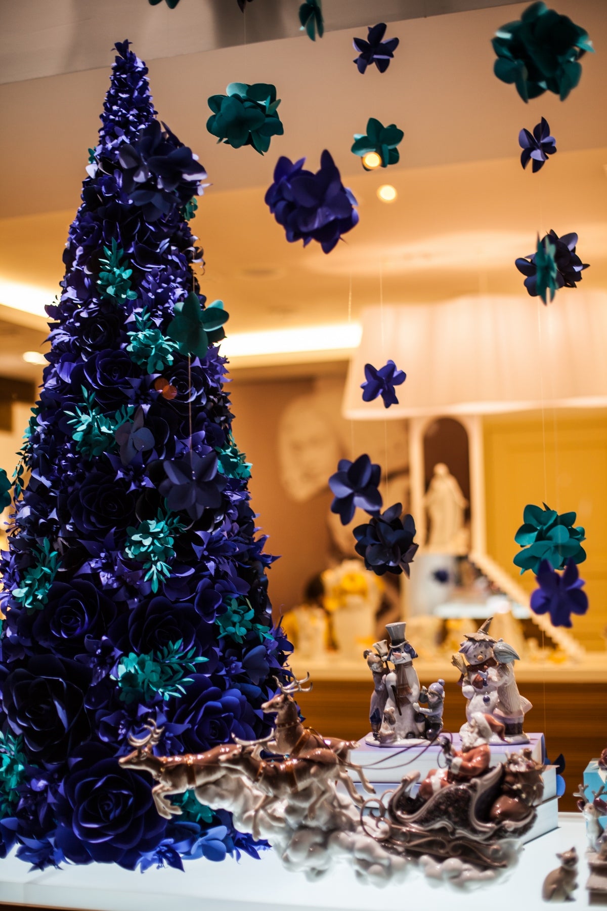 Vibrant paper flower art installation capturing the spirit of the holidays with a Christmas tree adorned in ultramarine blue and turquoise blue paper flowers and delicate hanging paper hydrangeas.