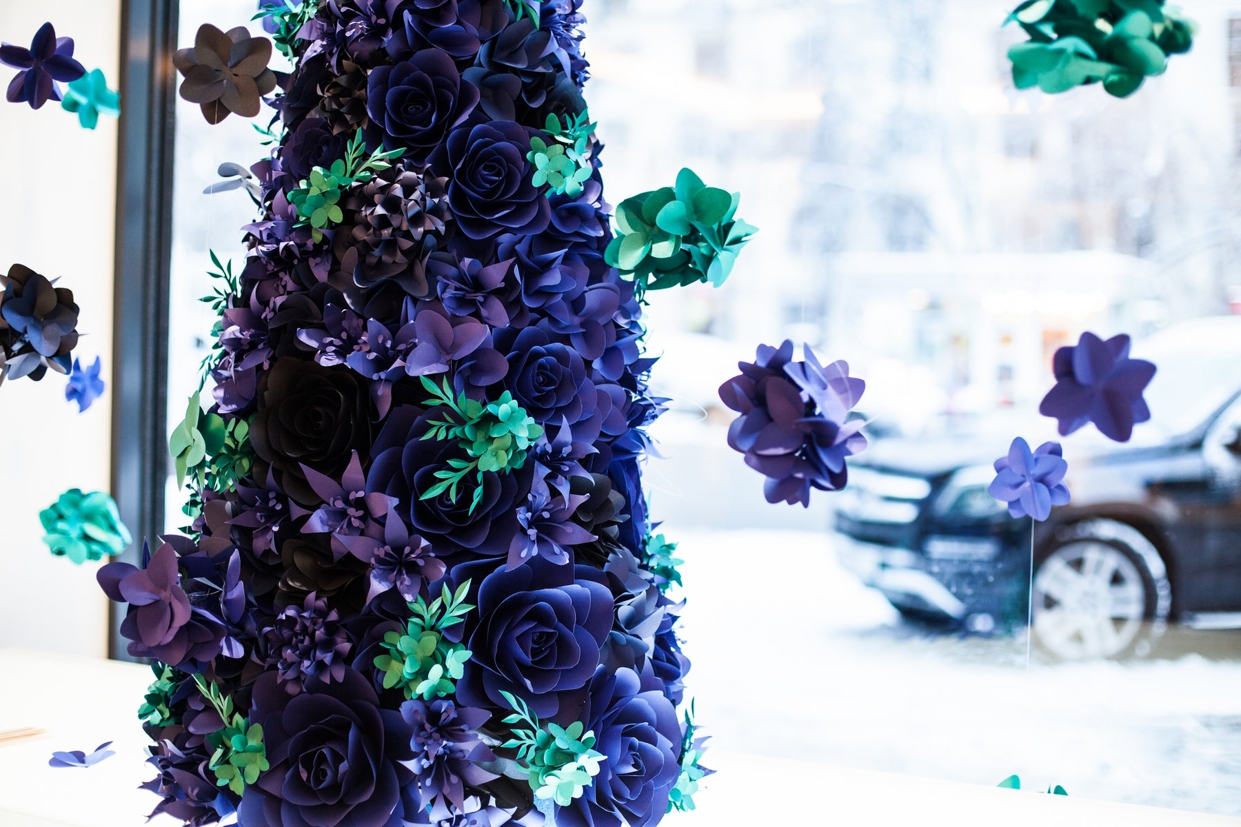 Installation d'arbre de Noël de fleurs en papier avec des fleurs en papier bleu outremer et bleu turquoise et des hortensias en papier suspendus, créant une vitrine d'hiver fantaisiste et élégante pour Lladró.