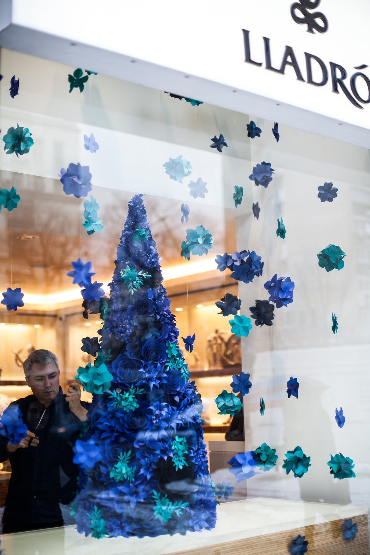 Whimsical paper flower installation featuring a Christmas tree adorned with ultramarine blue and turquoise blue paper flowers and hanging paper hydrangeas.