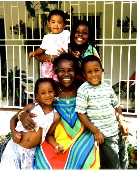 Teju's Jamaican Grandmother along with her young relatives smiling together in a big hug.