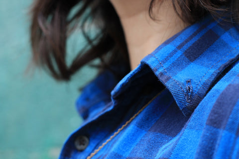 Close up of a blue flannel shirt collar with medium length brunette hair in the frame.