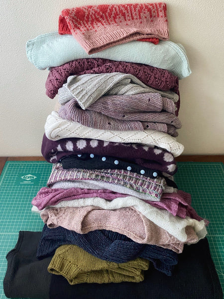 teetering pile of hand knit wool pullovers and sweaters