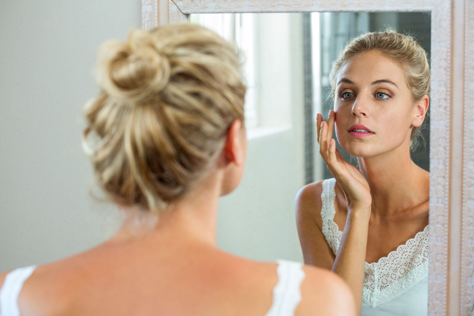 A woman looks in the mirror, touching her cheek and wondering, Does Neosporin help acne?