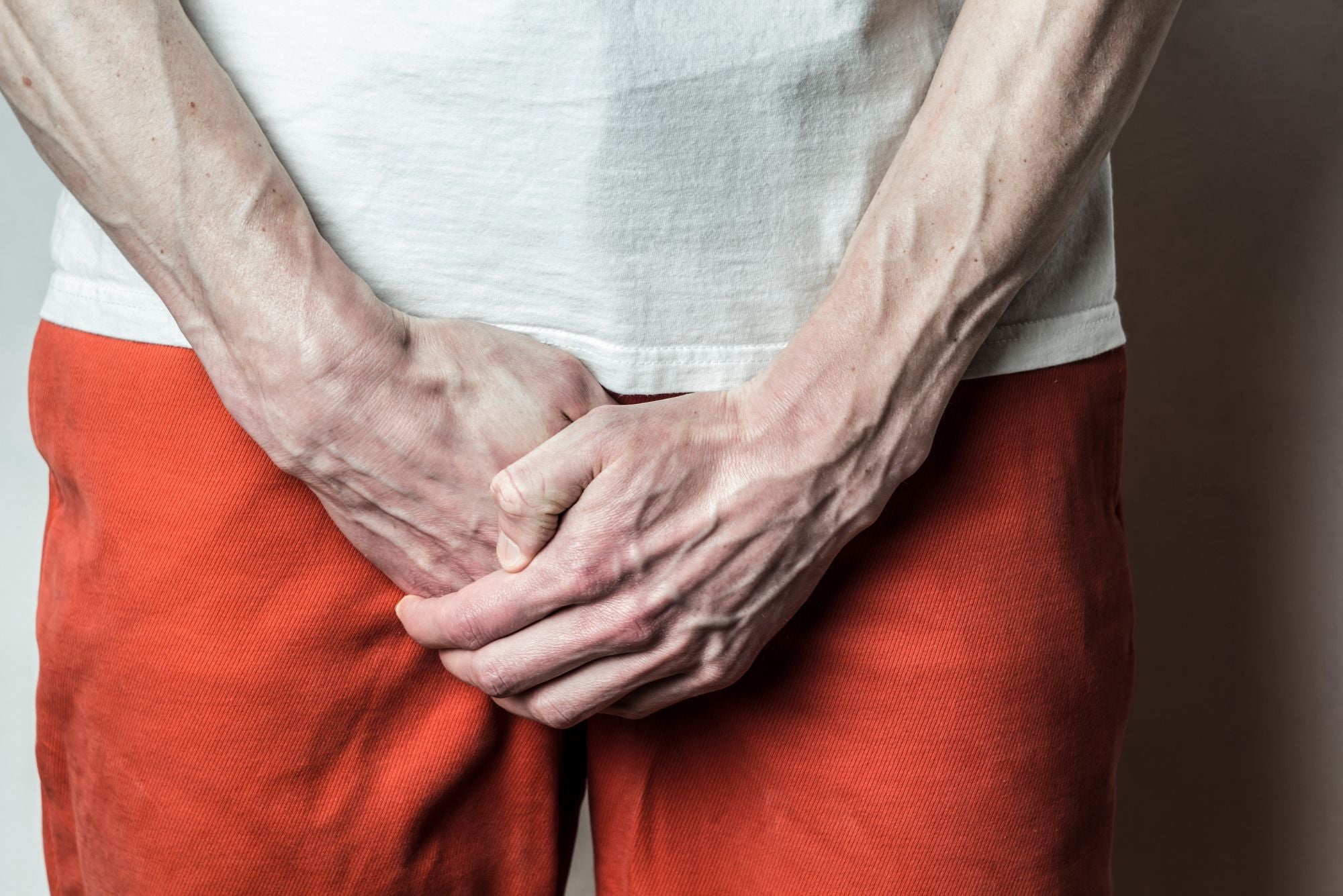 A person in orange pants and a white shirt holds their groin area, wondering if genital herpes is one bump or multiple bumps.