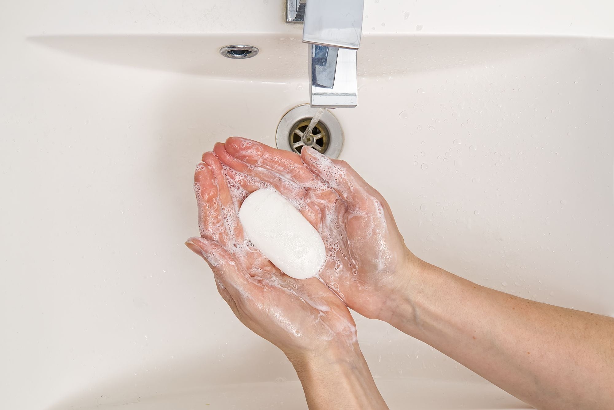 A woman holds a bar of acne antibacterial soap over a sink with running water.