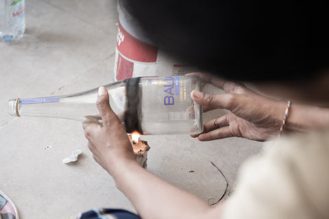 A woman using a candle to heat a Balian glass bottle to break it. 