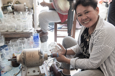 A woman smiling and sanding cut glass bottles to make into candle holders