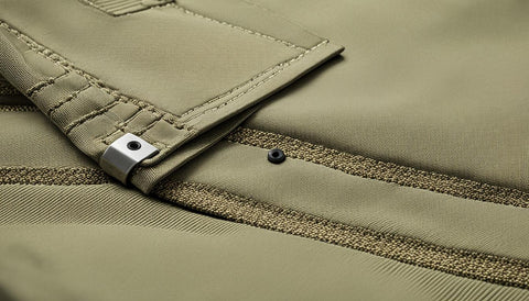 A close-up view of durable work pants with reinforced stitching and pockets. The fabric is thick and durable, yet breathable for comfort during long work hours. Show the pants in a neutral color, such as beige or khaki, and include subtle detailing like metal rivets and buttons. Place the pants on a flat surface, such as a wooden table or concrete floor, to emphasize their toughness and potential for daily use. Surround the pants with tools commonly used in manual labor jobs, such as hammers, wrenches, and screwdrivers. The overall tone should convey reliability and durability, while also highlighting the importance of safety and comfort in the workplace.