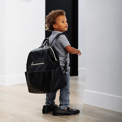 Cute afro-american toddler wearing his diaper bag on his back and funny. too big dad’s shoes on his feet