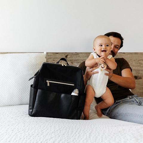 Dad holding smiling baby on the bed next to a diaper bag