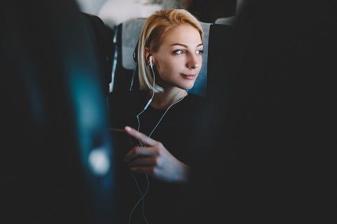 Beautiful young woman with short haircut listening favorite audio songs in modern earphones resting during flight and enjoying comfort first class sitting in seat on airplane board