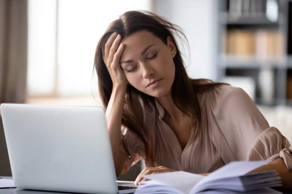 Mujer que muestra fatiga y dificultad para concentrarse mientras intenta trabajar en su computadora portátil