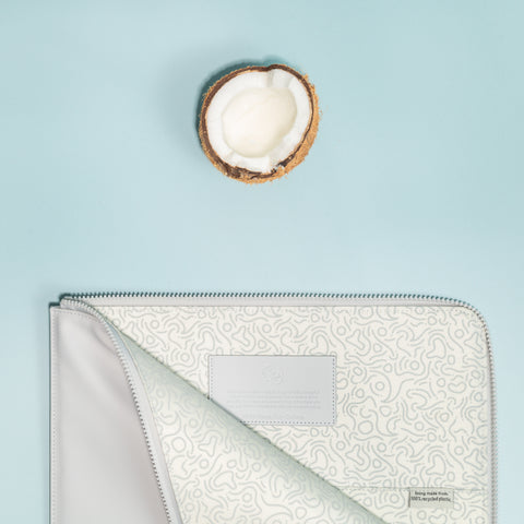 Birdseye image of the OneNine5 eco laptop sleeve zipped open. Above is half a coconut open, showing the inner white flesh