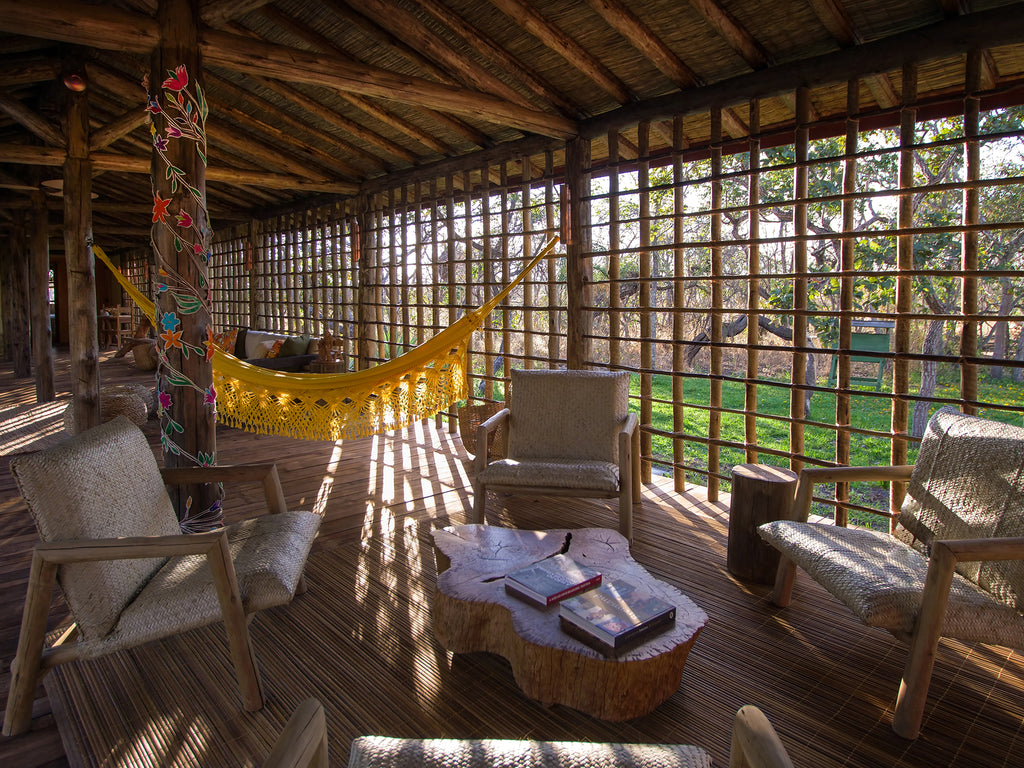 Inside the ecologeg, Pousada Trijunção in Brazil. Natural sunlight illuminates a relaxed seat area made up of comfortable chairs and a hammock.