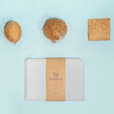 Birdseye image of the grey OneNine5 Coconut Padded Laptop Sleeve, packaged in a recycled kraft paper sleeve. Above the laptop cases is a coconut and the coconut fibres that are formed into a padding to protect a laptop or MacBook