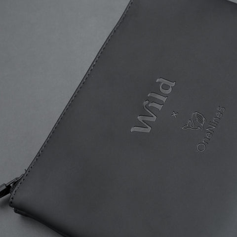 Closeup of Wild x OneNine5 debossed logo on the black, vegan leather pouch.