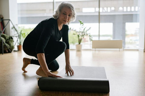 elder woman laying out a yoga mat in studio