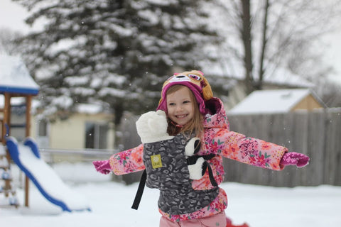 Child playing in snowing yard with a doll in a play baby carrier