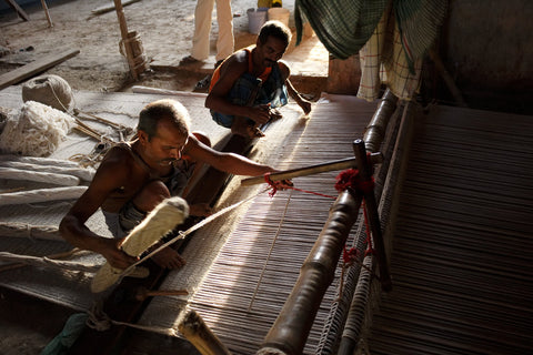 Two men in India weaving a rug on a traditional loom. 