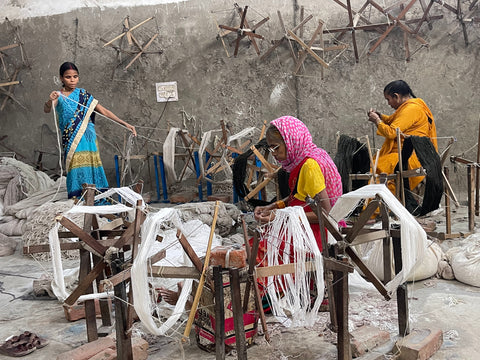 Indian women in brightly colored saris combining many strands of yarn together for weaving a rug.