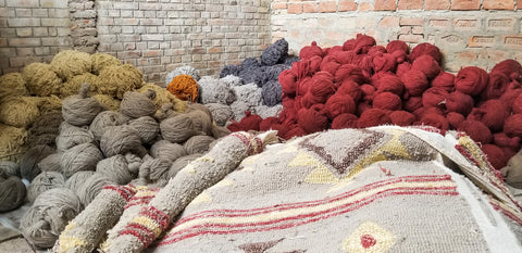Pile of wool rug yarn and a rolled up rug.