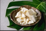 Image of pieces of cocoa butter in a brown bowl on a wide green leaf