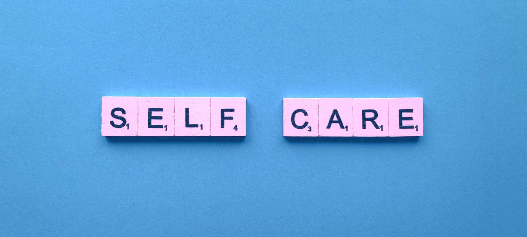 Pink letter tiles that read self-care against a blue background