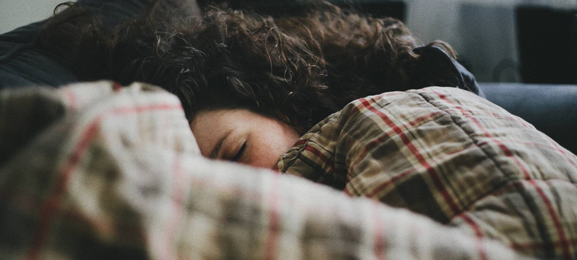 Curly haired woman taking a nap on a couch with a blanket