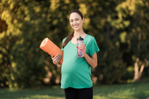 a pregnant woman holding a tumbler with water after exercising outdoors