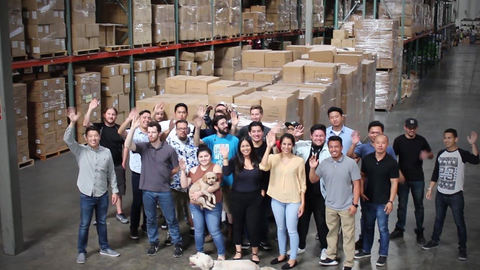 Entire warehouse team waving to camera in large warehouse