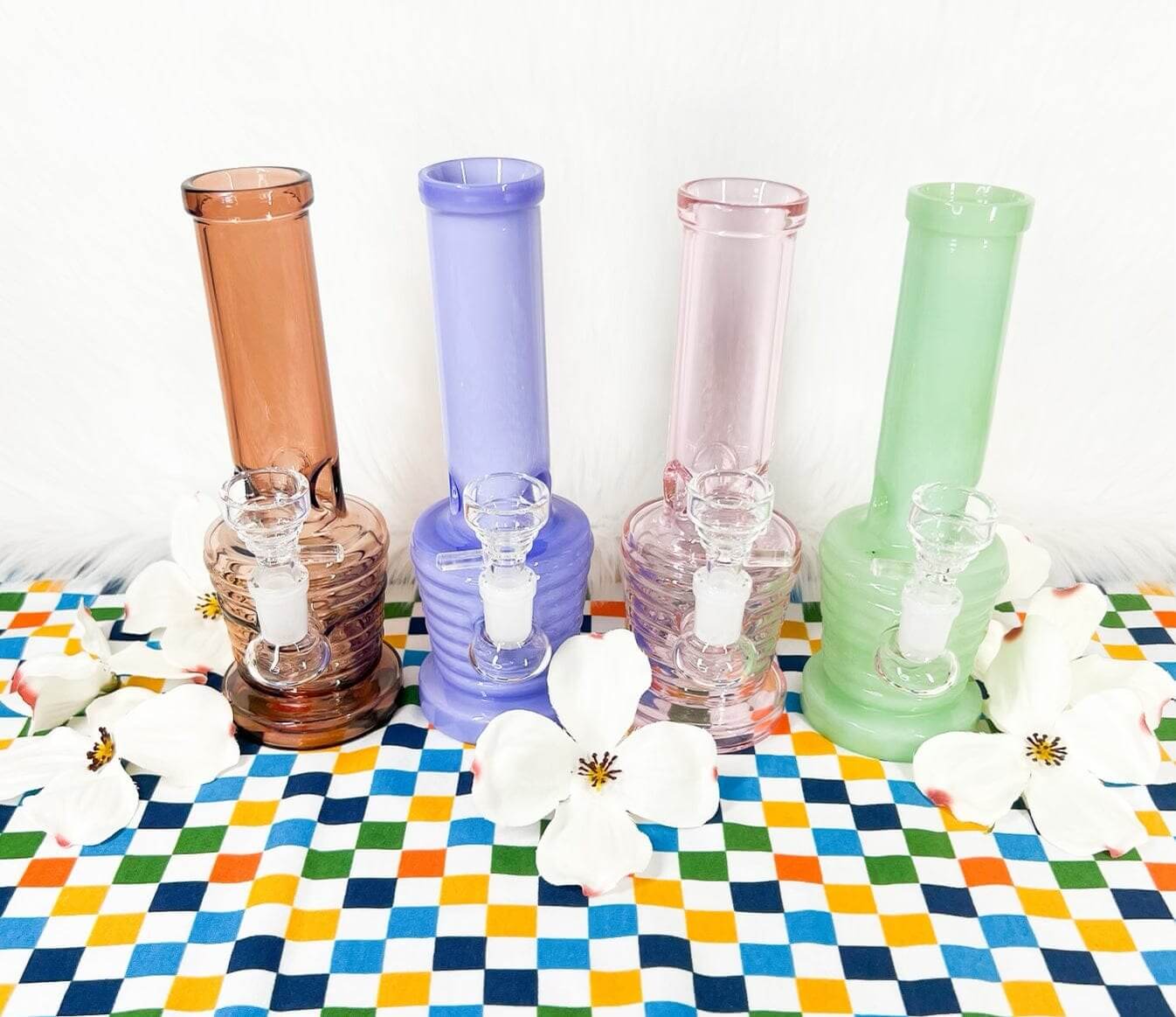 four modern glass dab rigs and white flowers on a checkered print tablecloth
