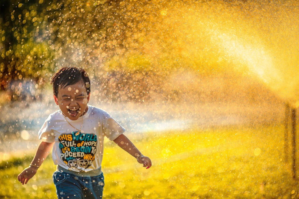 Happy child running through a sprinkler