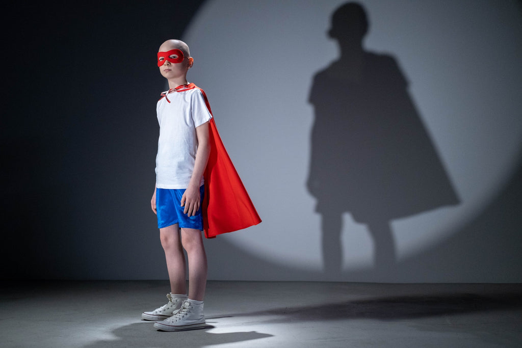 A little boy dressed up as a superhero with his shadow behind him on a wall.