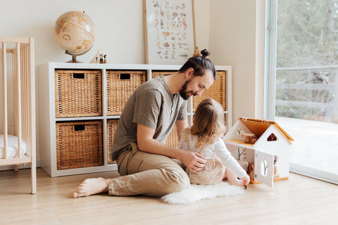 A father and his daughter playing with a dollhouse.