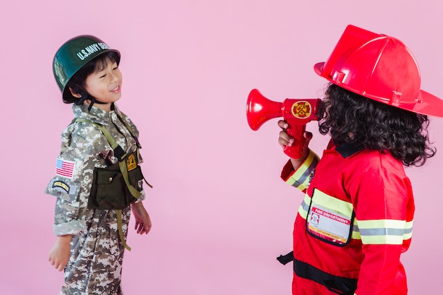 A boy in a soldier costume and a girl in a firefighter one representing the best gift ideas for kids who love to pretend play.