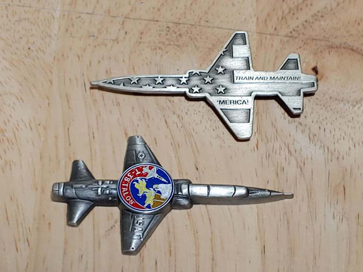  Challenge coins shaped like a fighter plane that says “Train and Maintain ‘ Merica” on the back.