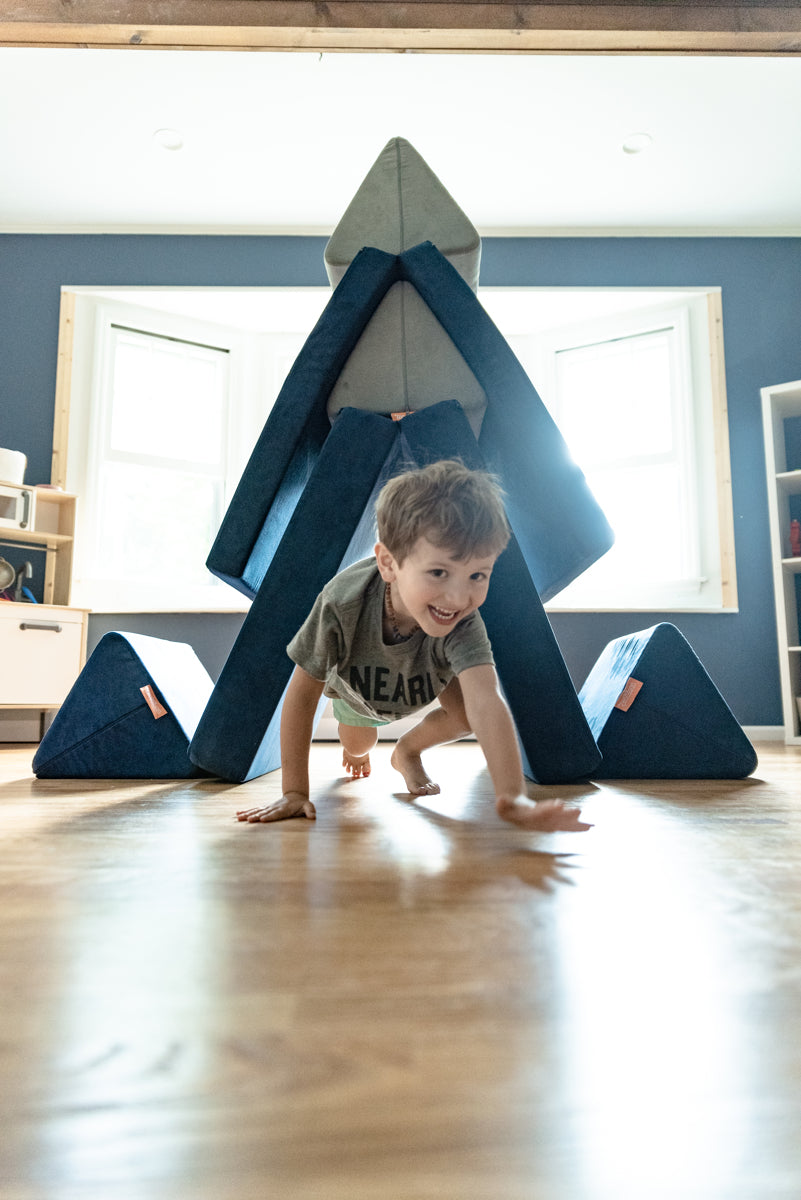 Child crawling toward the camera, out of a Nugget fort
