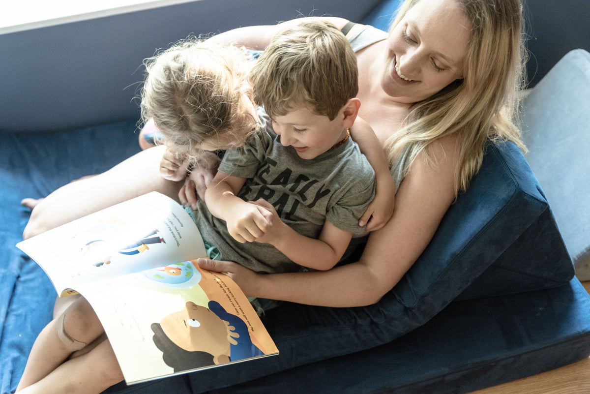 Adult and two children sitting on a Nugget, reading a story together