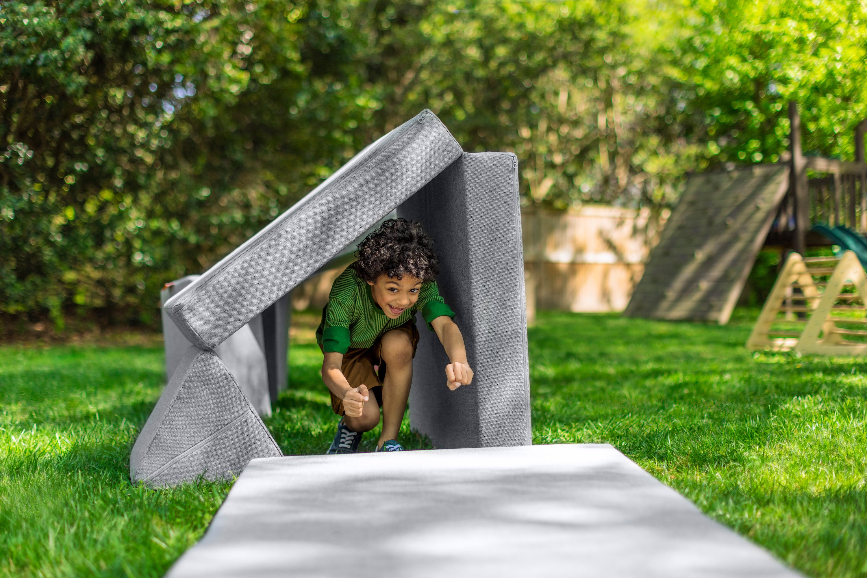 A child runs through a Nugget obstacle course tunnel on a bright green lawn