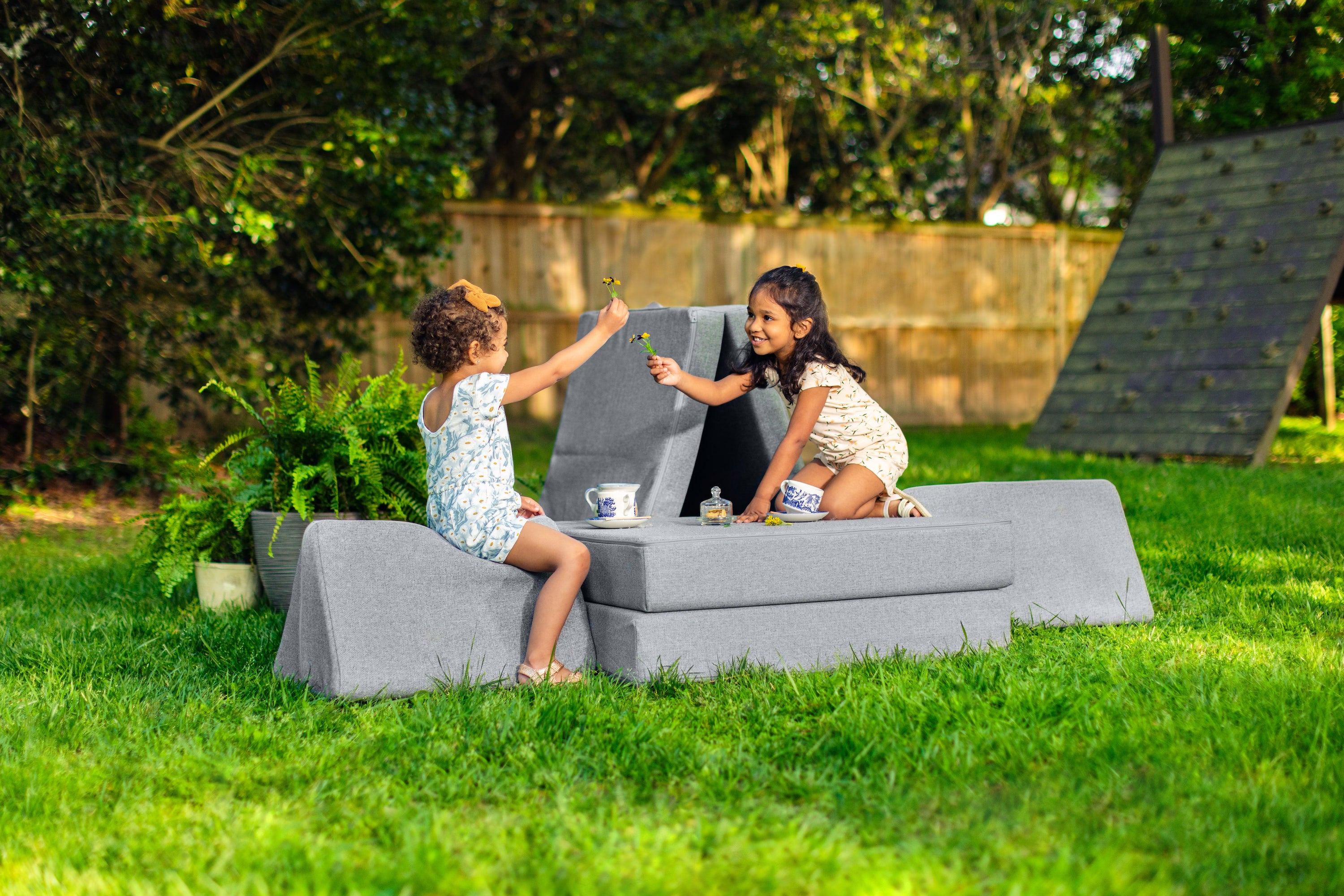 Two children sit on an Outdoor Nugget set up as a table and chairs, enjoying a tea party in the backyard