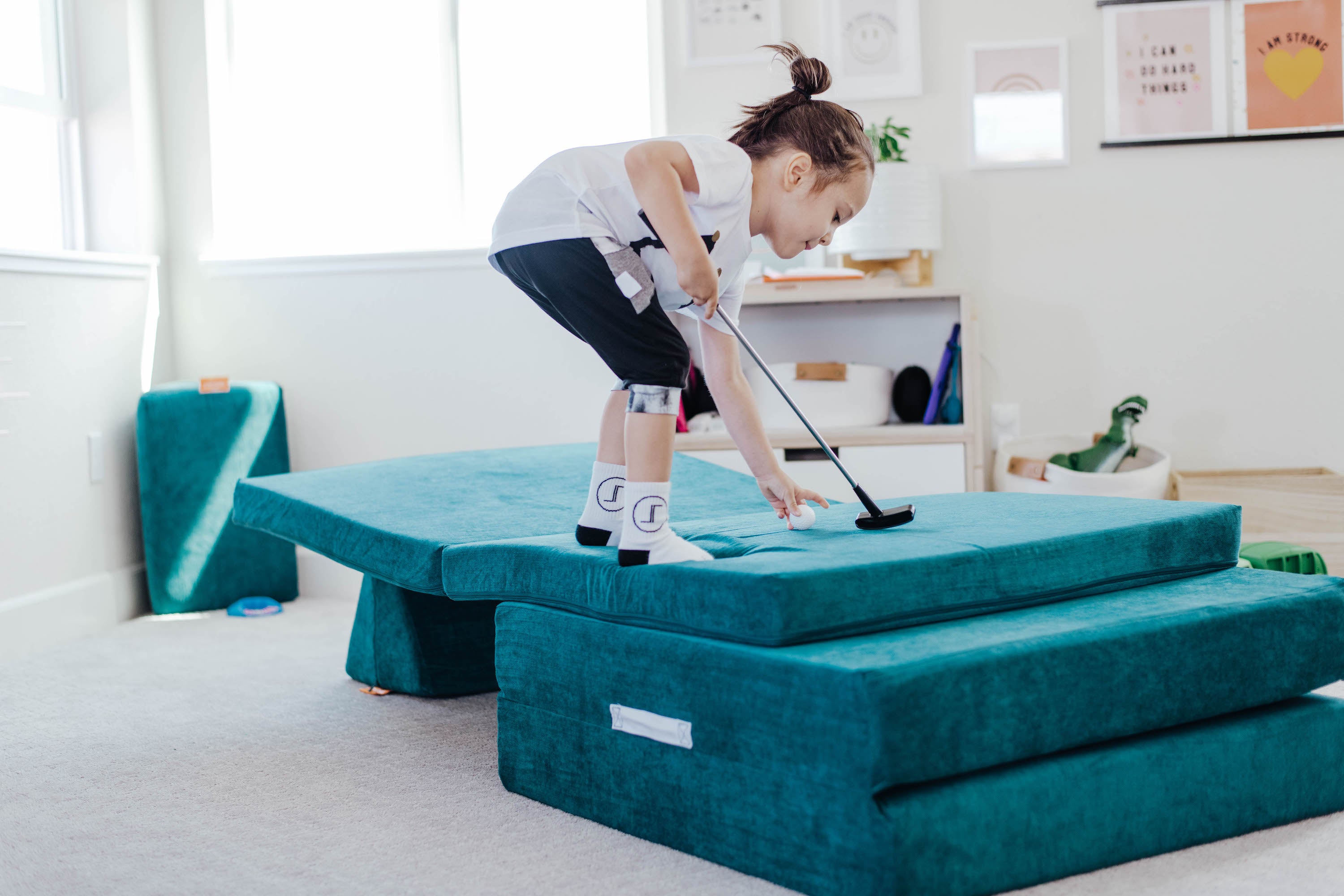 Child sets up for mini-golf on a Nugget, with tiers of base, cushion, and pillows.