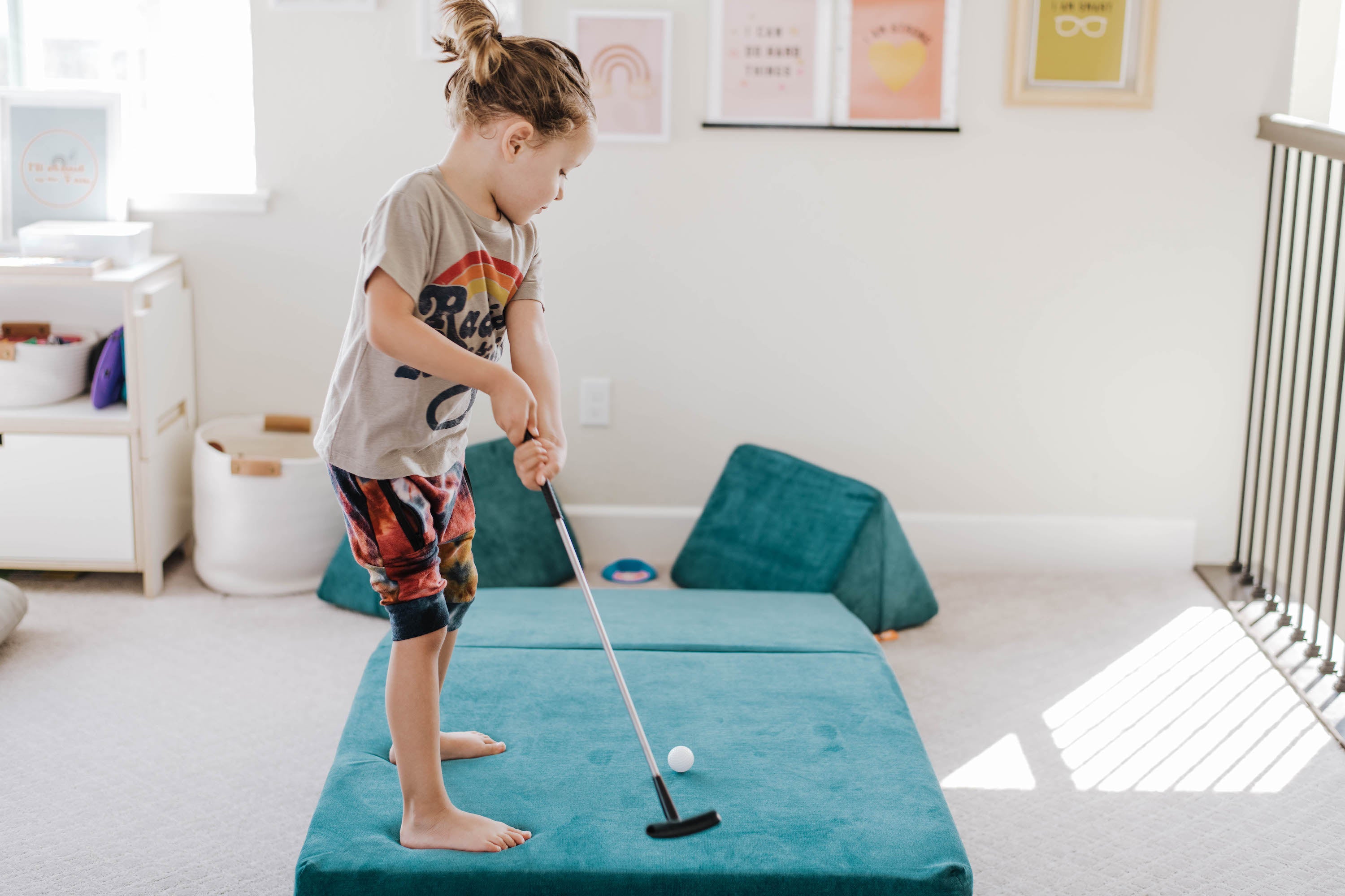 Child standing on an Atlantis Nugget, holding a golf club and aiming for a "hole" between two Nugget pillows