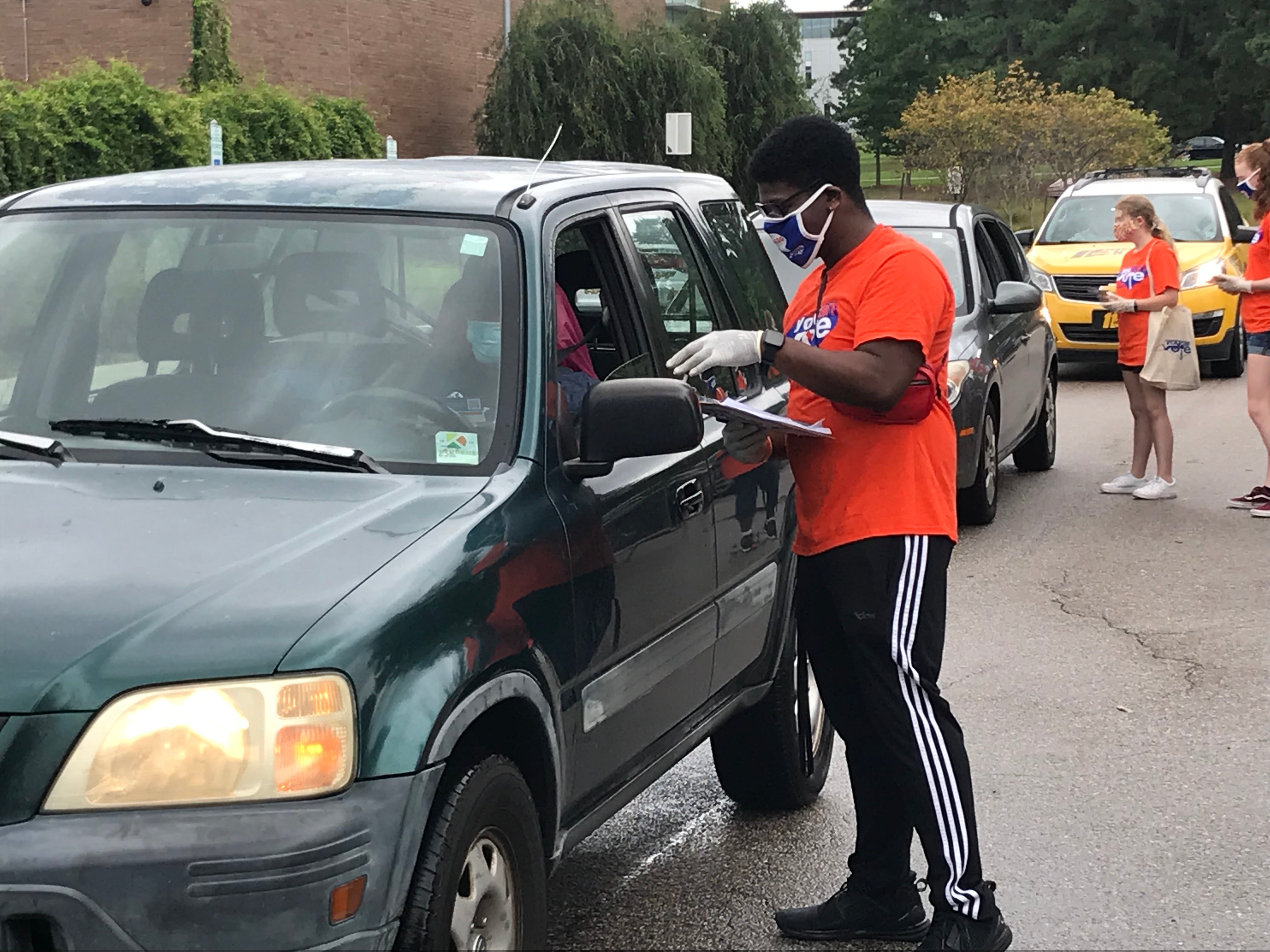Voter registration drive, with volunteer standing alongside a car with clipboard, helping individual register to vote