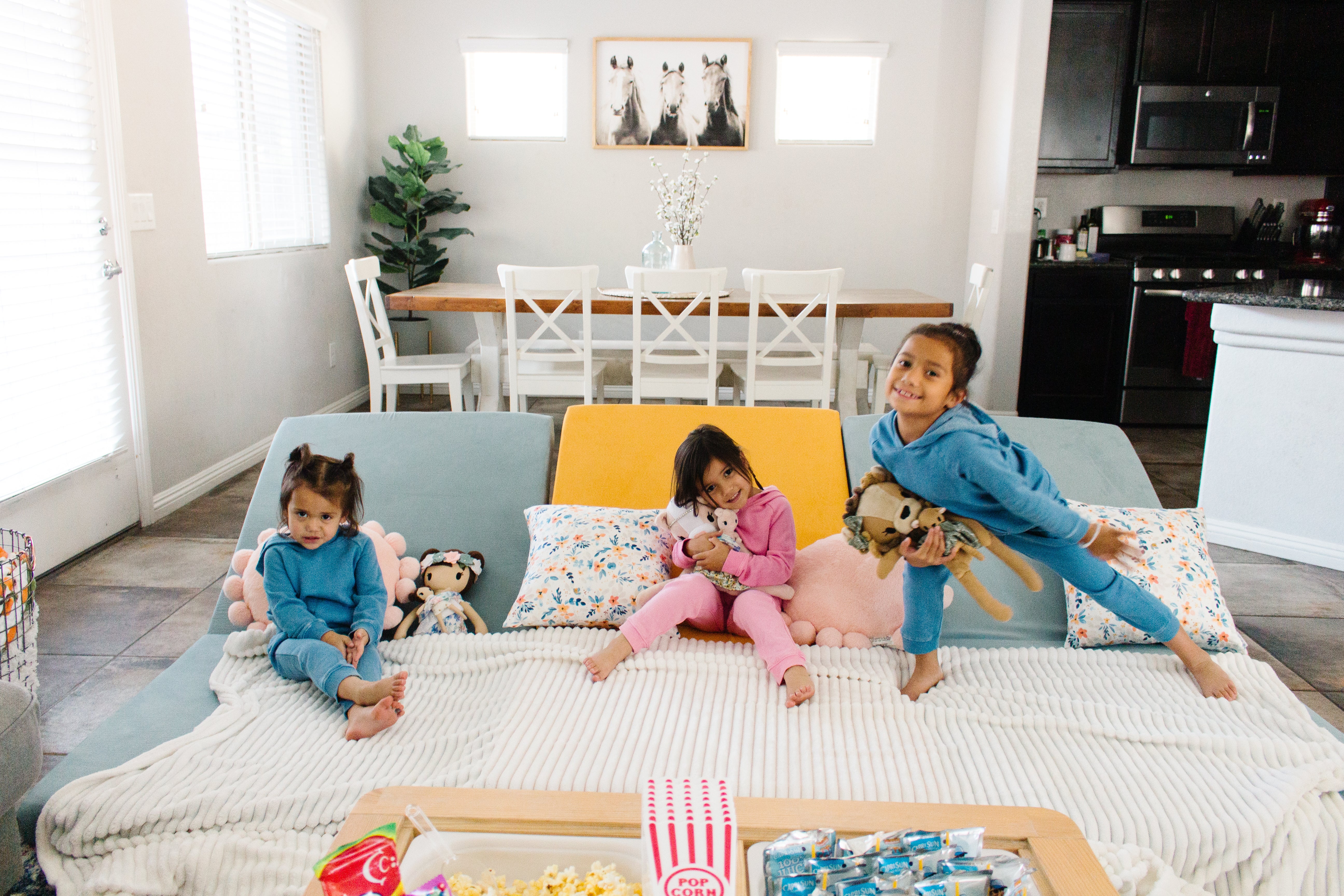 Three Nugget couches pushed up against each other for movie watching; three kids lounging and standing on their own areas