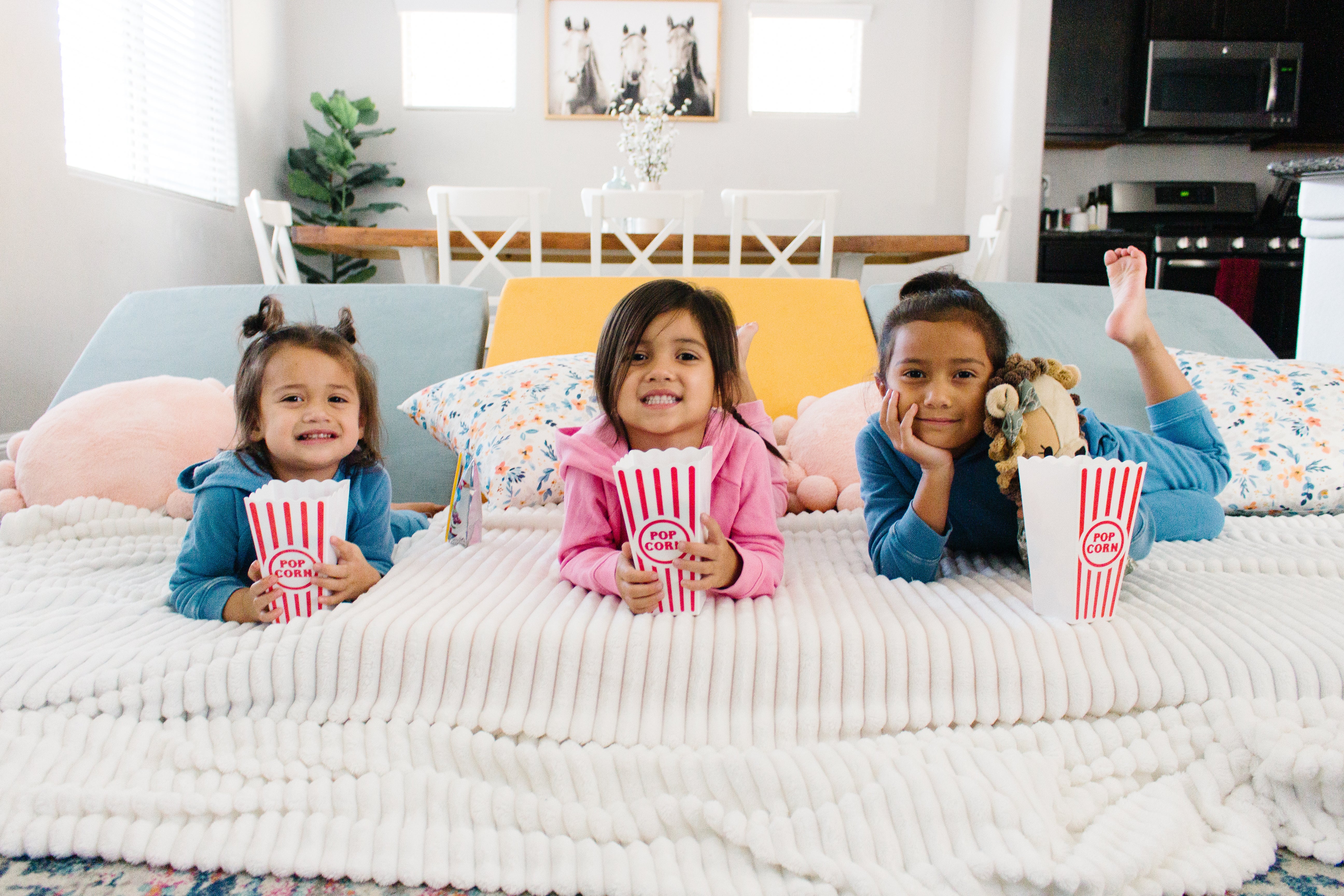 Three kids ready for movie night, popcorn containers in hand and Nugget couches set up as one big pallet