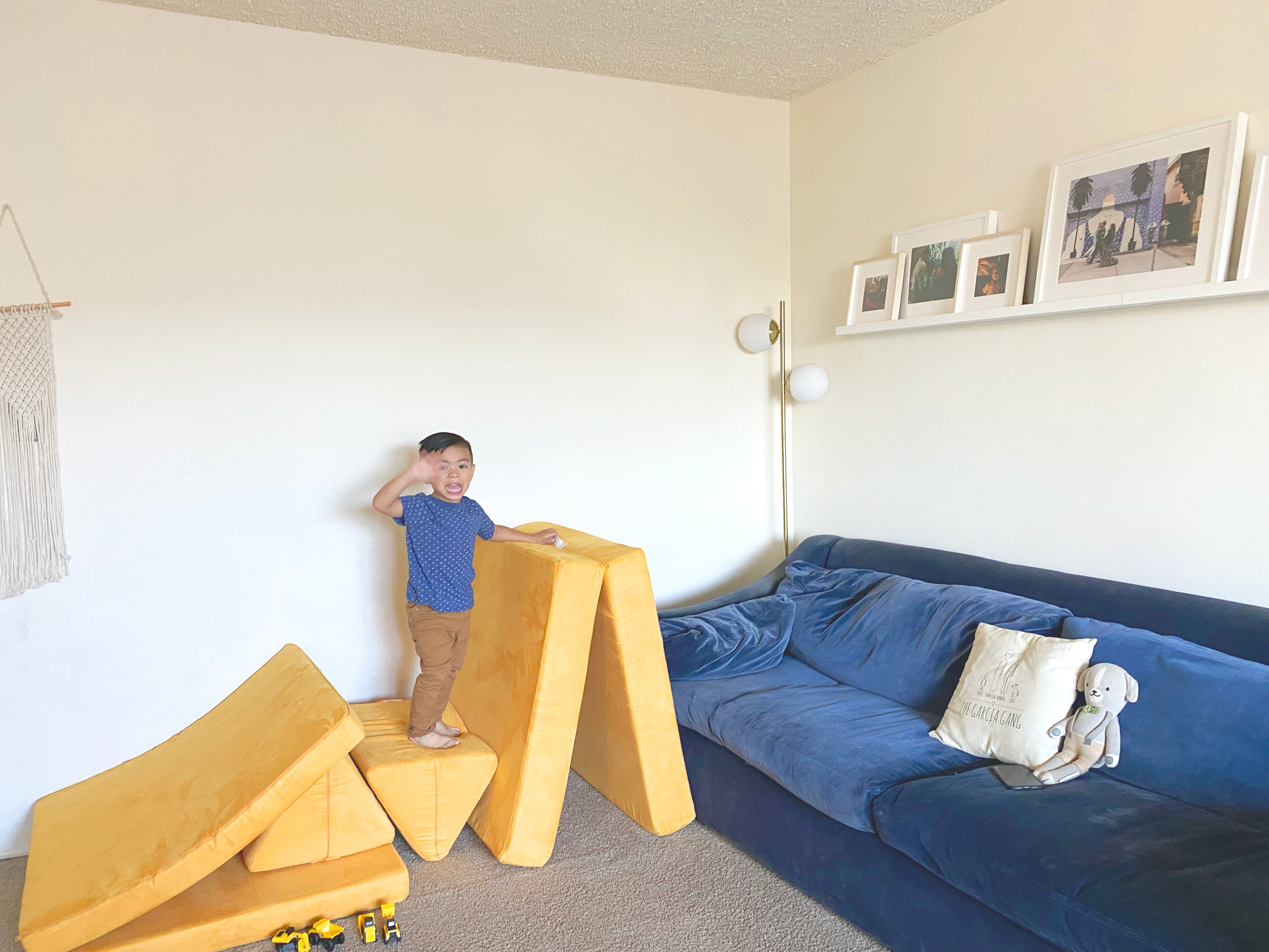 Child standing on a Nugget build waving at camera. Cushion is folded over a pillow, placed next to a tented base.