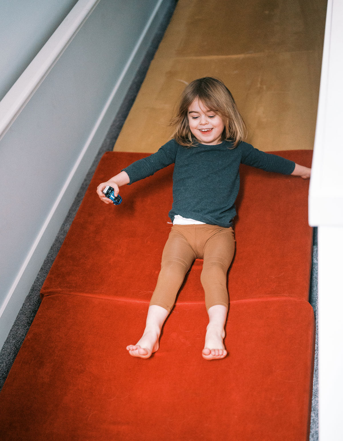 A child smiles as they slide down a Nugget stairway slide.